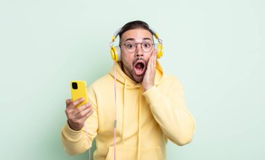 Genç ve yakışıklı bir adam şok olmuş ve korkmuş hissediyor. kulaklıklar ve akıllı telefon konsepti
