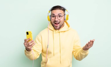 Genç yakışıklı adam kendini mutlu hissediyor, bir çözüm ya da fikir bulduğuna şaşırıyor. kulaklıklar ve akıllı telefon konsepti
