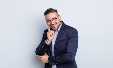 Genç ve yakışıklı bir adam mutlu ve kendinden emin bir ifadeyle gülümsüyor, elleri çenesinde. İş adamı konsepti