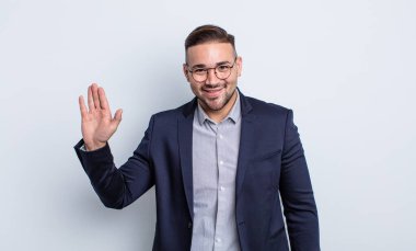 Genç yakışıklı adam mutlu bir şekilde gülümsüyor, el sallıyor, sizi selamlıyor ve selamlıyor. İş adamı konsepti