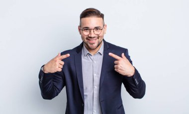 Genç ve yakışıklı bir adam kendi gülüşünü işaret ederek kendine güvenerek gülümsüyor. İş adamı konsepti