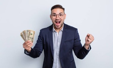 Genç yakışıklı adam kendini mutlu hissediyor ve inanılmaz bir şeye hayret ediyor. Dolar banknotları konsepti