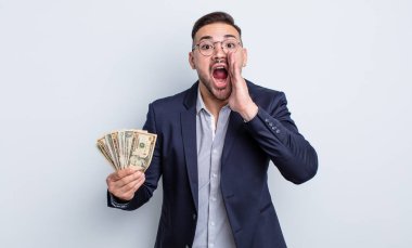 Genç yakışıklı adam mutlu hissediyor, elleri ağzının kenarında bağırıyor. Dolar banknotları konsepti