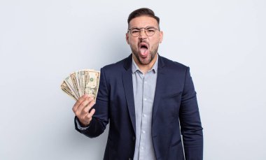 Genç ve yakışıklı bir adam tiksinmiş ve sinirlenmiş hissediyor ve dilini dışarı çıkarıyor. Dolar banknotları konsepti