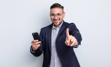 Genç yakışıklı adam gülümsüyor ve arkadaş canlısı görünüyor. Bir numaralı iş ve akıllı telefon konseptini gösteriyor.