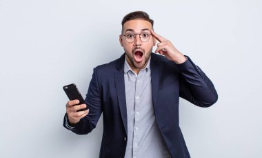 Genç yakışıklı adam şaşırmış görünüyor, yeni bir düşünce, fikir ya da konsept iş ve akıllı telefon kavramının farkına varıyor.