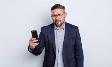 Genç yakışıklı adam kafası karışmış, kafası karışmış iş ve akıllı telefon kavramı arıyor.