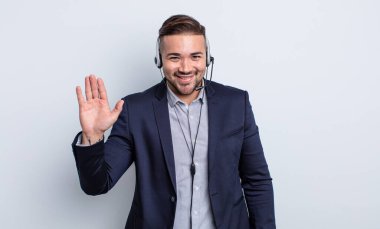 Genç yakışıklı adam mutlu bir şekilde gülümsüyor, el sallıyor, sizi selamlıyor ve selamlıyor. Tele pazarlamacı kavramı