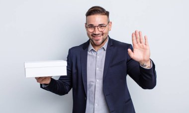 Genç yakışıklı adam mutlu bir şekilde gülümsüyor, el sallıyor, sizi selamlıyor ve selamlıyor. beyaz kutu kavramı