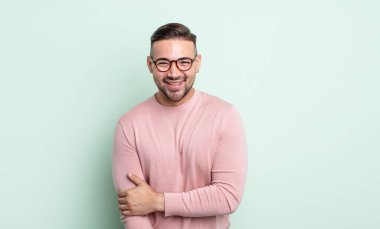 Genç yakışıklı adam utangaç ve neşeli bir şekilde gülüyor, arkadaş canlısı ve olumlu ama güvensiz bir tavırla.