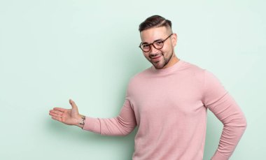 Genç yakışıklı adam kendini mutlu ve neşeli hissediyor, gülümsüyor ve seni selamlıyor, dostça bir jestle içeri davet ediyor.