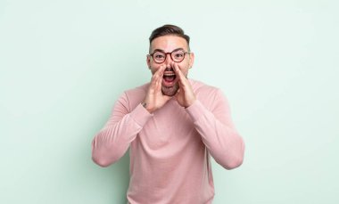 Genç yakışıklı adam mutlu, heyecanlı ve pozitif hissediyor. Elleri ağızda, bağırıyor.