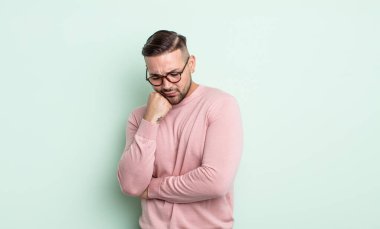 Genç yakışıklı adam ciddi, düşünceli ve endişeli, elleri çenesine bastırılmış, yan bakıyor.