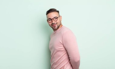 Genç yakışıklı adam neşeyle gülümsüyor, mutlu, tatmin olmuş ve rahatlamış hissediyor, kollarını kavuşturup yan tarafa bakıyor.