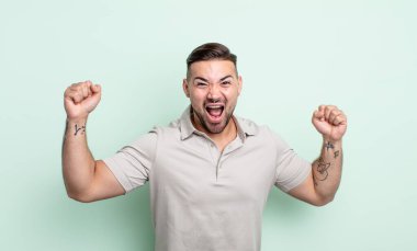 Genç yakışıklı adam zaferle bağırıyor. Heyecanlı, mutlu ve şaşırmış görünüyor. Kutlama yapıyor.