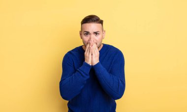Genç yakışıklı adam endişeli, üzgün ve korkmuş, elleri ağızda, endişeli ve berbat görünüyor.