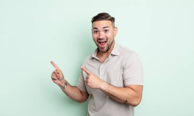 Genç, yakışıklı bir adam kendini neşeli ve şaşırmış hissediyor. Şok olmuş bir ifadeyle gülümsüyor ve bir tarafı işaret ediyor.