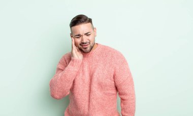 Genç yakışıklı adam yanağını tutuyor ve ağrılı diş ağrısı çekiyor, hasta, sefil ve mutsuz hissediyor, dişçi arıyor.