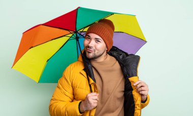 Genç yakışıklı adam kibirli, başarılı, pozitif ve gururlu görünüyor. yağmur ve şemsiye kavramı