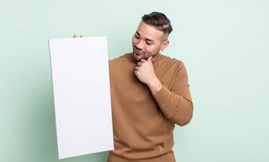 Genç ve yakışıklı bir adam mutlu ve kendinden emin bir ifadeyle gülümsüyor, elleri çenesinde. boş tuval kavramı