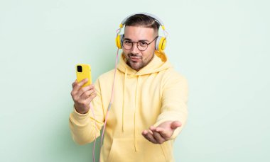 Genç ve yakışıklı bir adam arkadaşça gülümsüyor ve bir konsept sunuyor. kulaklıklar ve akıllı telefon konsepti