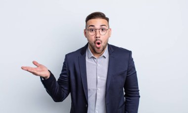 Genç, yakışıklı adam şaşırmış ve şok olmuş görünüyor. Çenesi düşmüş, elinde bir nesne var. İş adamı konsepti