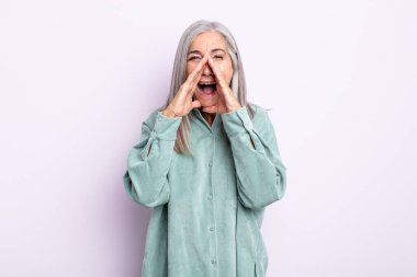 Orta yaşlı beyaz saçlı kadın mutlu, heyecanlı ve pozitif hissediyor, elleri ağızlarının yanında bağırıyor, bağırıyor