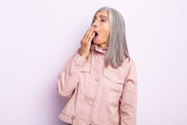 Orta yaşlı beyaz saçlı kadın sabahın erken saatlerinde uyanıyor, uykulu, yorgun ve sıkkın görünüyor.