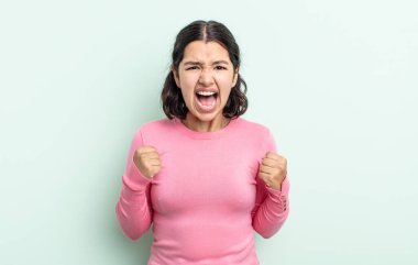 Güzel genç bir kadın sinirli, sinirli, kızgın bakışlar ve sıkı yumruklar ile agresif bir şekilde bağırıyor.