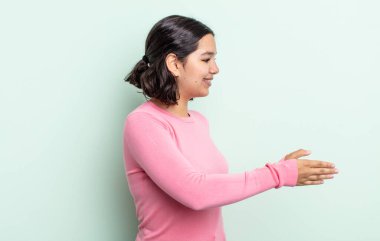 Güzel genç bir kadın gülümsüyor, seni selamlıyor ve başarılı bir anlaşma için el sıkışmayı teklif ediyor, işbirliği konsepti.