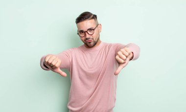 Genç yakışıklı adam üzgün, hayal kırıklığına uğramış ya da kızgın görünüyor, anlaşmazlık içinde baş parmağını gösteriyor, hayal kırıklığına uğramış hissediyor.