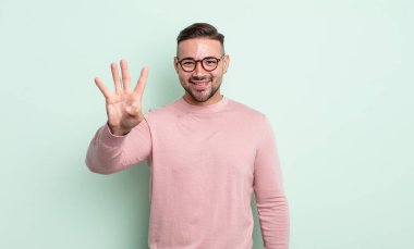 Genç yakışıklı adam gülümsüyor ve arkadaş canlısı görünüyor, 4 ya da 4 numarayı gösteriyor, eli önde, geri sayıyor.