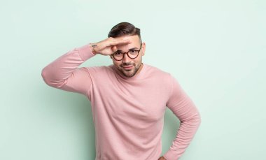 Genç yakışıklı adam şaşkın ve şaşkın bakıyor, el üstünde uzak bakıyor, izliyor ya da arıyor