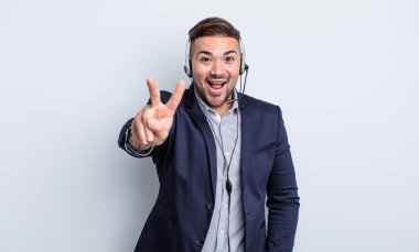 Genç yakışıklı adam gülümsüyor ve mutlu görünüyor, zafer ya da barış işareti yapıyor. Tele pazarlamacı kavramı