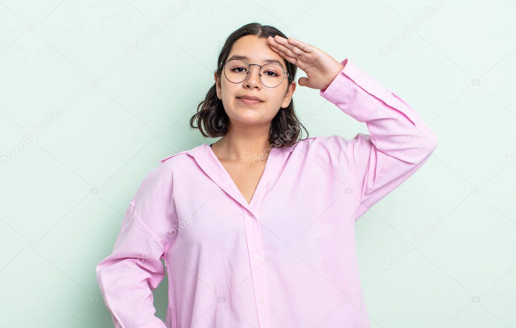 pretty teenager woman greeting the camera with a military salute in an act of honor and patriotism, showing respect