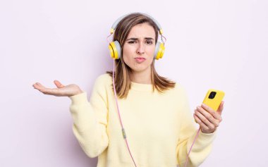 Genç ve güzel bir kadın şaşkın, şaşkın ve şüpheci hissediyor. kulaklıklar ve telefon konsepti