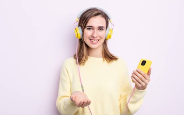 Genç ve güzel bir kadın arkadaşça gülümsüyor ve bir konsept sunuyor. kulaklıklar ve telefon konsepti