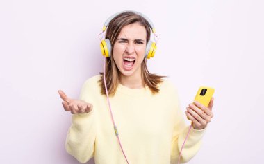 Genç ve güzel bir kadın sinirli, sinirli ve sinirli görünüyor. kulaklıklar ve telefon konsepti