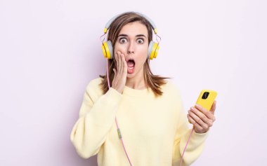 Genç ve güzel bir kadın şok olmuş ve korkmuş hissediyor. kulaklıklar ve telefon konsepti