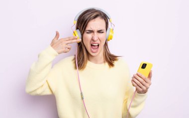 Genç ve güzel bir kadın mutsuz ve stresli görünüyor, intihar jesti silah işareti yapıyor. kulaklıklar ve telefon konsepti