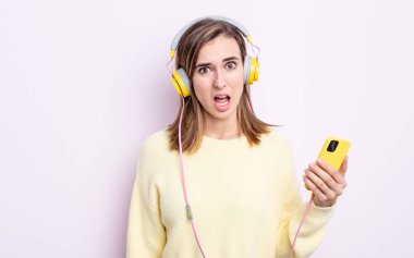 Genç ve güzel bir kadın şaşkın ve şaşkın hissediyor. kulaklıklar ve telefon konsepti