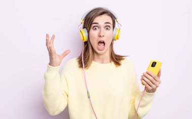 Genç ve güzel bir kadın ellerini havaya kaldırarak çığlık atıyor. kulaklıklar ve telefon konsepti