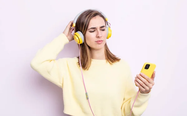 若い女性は困惑して混乱して頭を掻いてる ヘッドフォンと電話のコンセプト — ストック写真