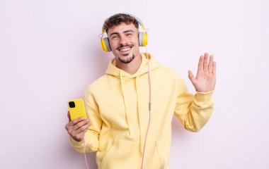 Genç yakışıklı adam mutlu bir şekilde gülümsüyor, el sallıyor, sizi selamlıyor ve selamlıyor. müzik konsepti
