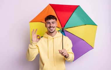 Genç yakışıklı adam kendini mutlu hissediyor, iyi bir jestle onaylıyor. şemsiye kavramı