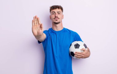 Genç ve yakışıklı adam ciddi görünüyor. Avuç içi gösteriyor. Durdurma hareketi yapıyor. futbol kavramı