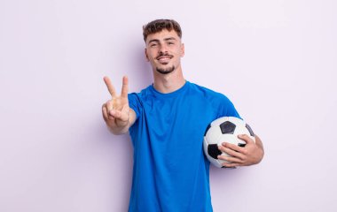 Genç yakışıklı adam gülümsüyor ve arkadaş canlısı görünüyor, iki numarayı gösteriyor. futbol kavramı