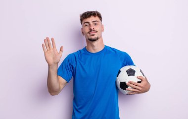 Genç yakışıklı adam mutlu bir şekilde gülümsüyor, el sallıyor, sizi selamlıyor ve selamlıyor. futbol kavramı