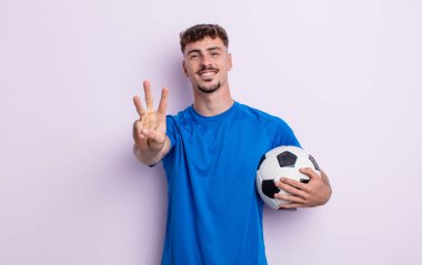 Genç yakışıklı adam gülümsüyor ve arkadaş canlısı görünüyor, üç numarayı gösteriyor. futbol kavramı