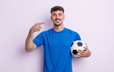 Genç ve yakışıklı bir adam kendi gülüşünü işaret ederek kendine güvenerek gülümsüyor. futbol kavramı